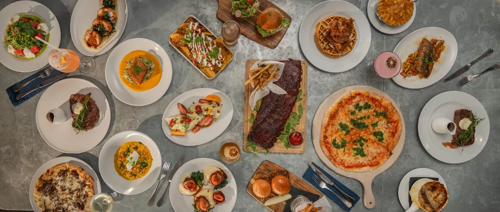 Overhead view of a large spread of diverse restaurant food and drinks.