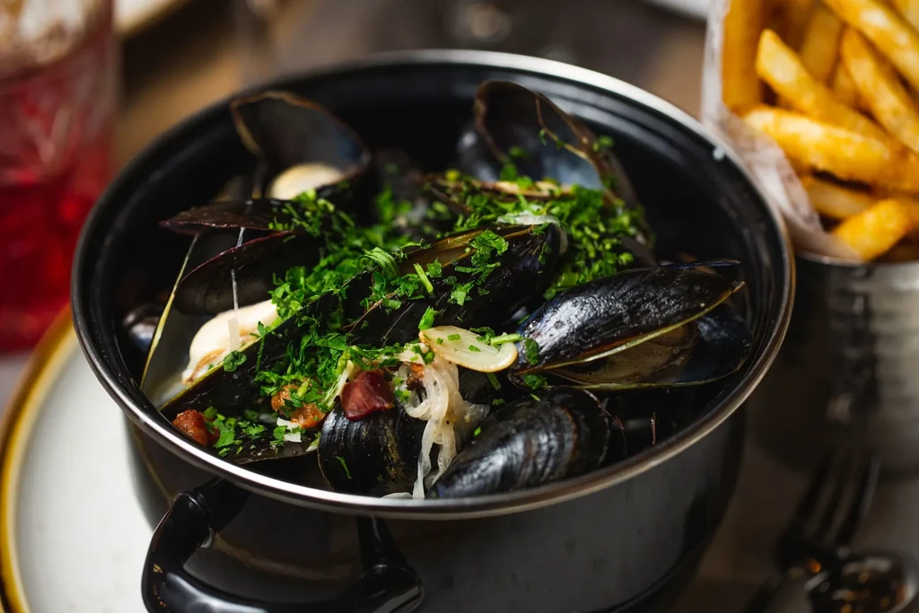 Steamed mussels in a cast-iron pot with fries and a red drink.