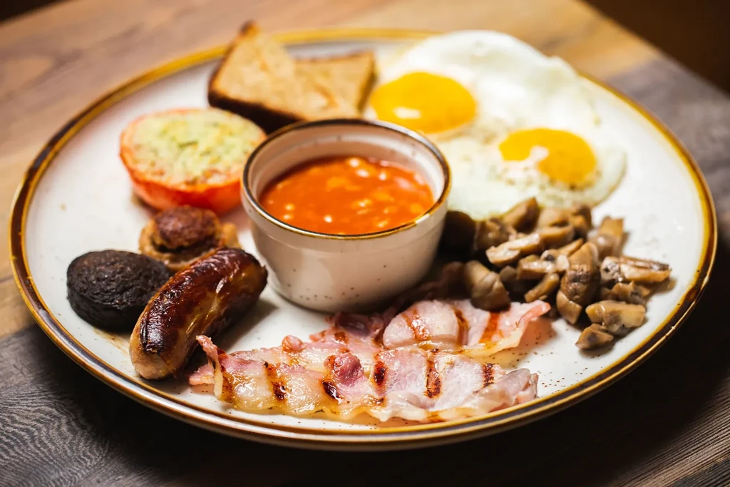 A full English breakfast with fried eggs, bacon, sausage, and beans.