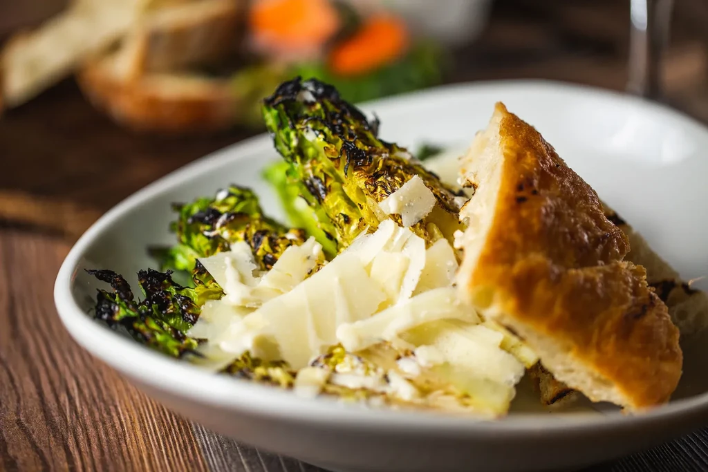 Charred romaine lettuce, cheese shavings, and bread in a white bowl.