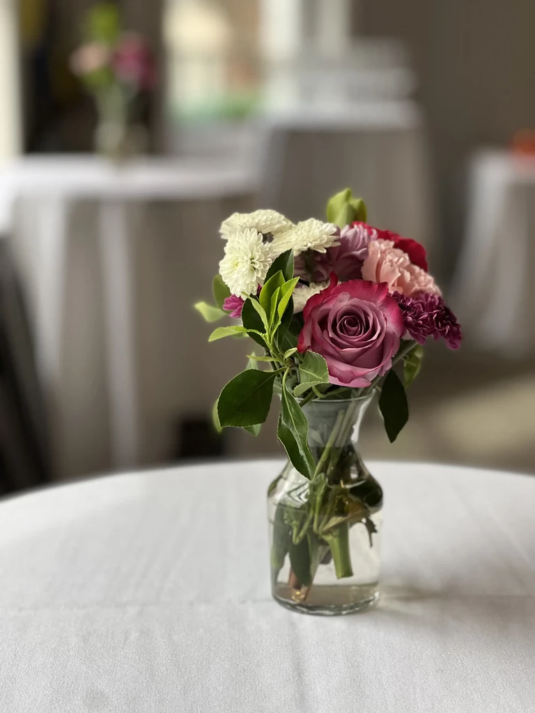 Elegant mixed floral arrangement in clear vase on white tablecloth.