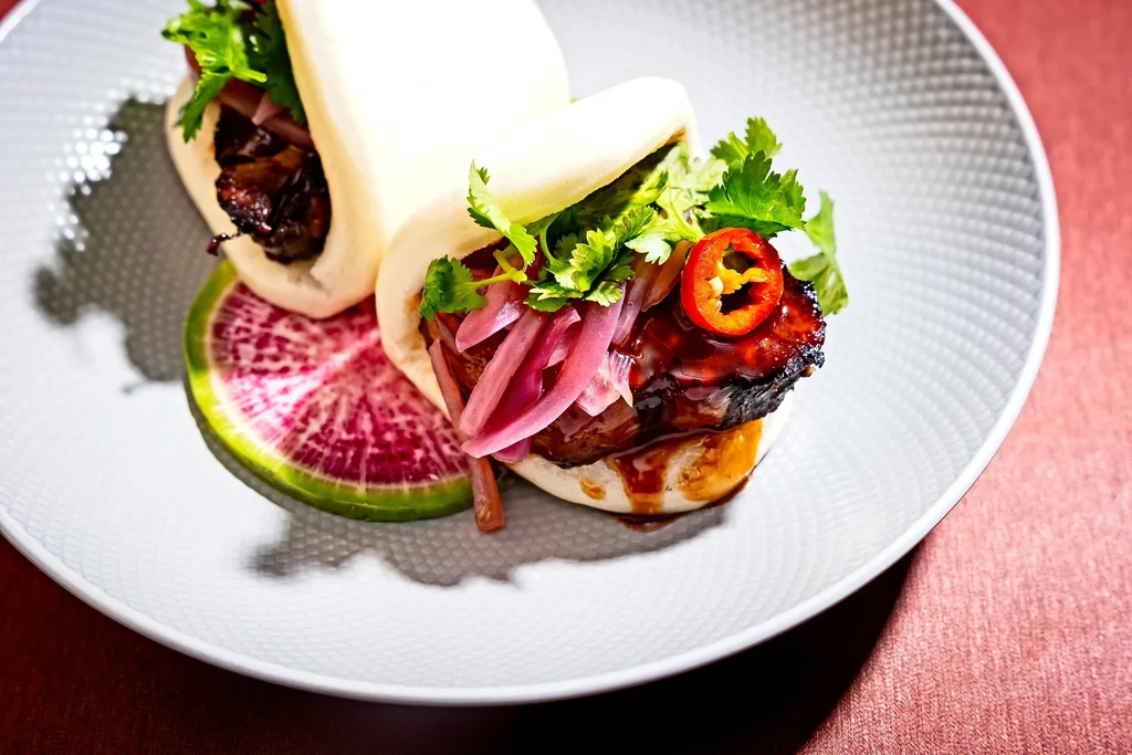 Two bao buns with glazed pork, pickled onions, cilantro, and radish.