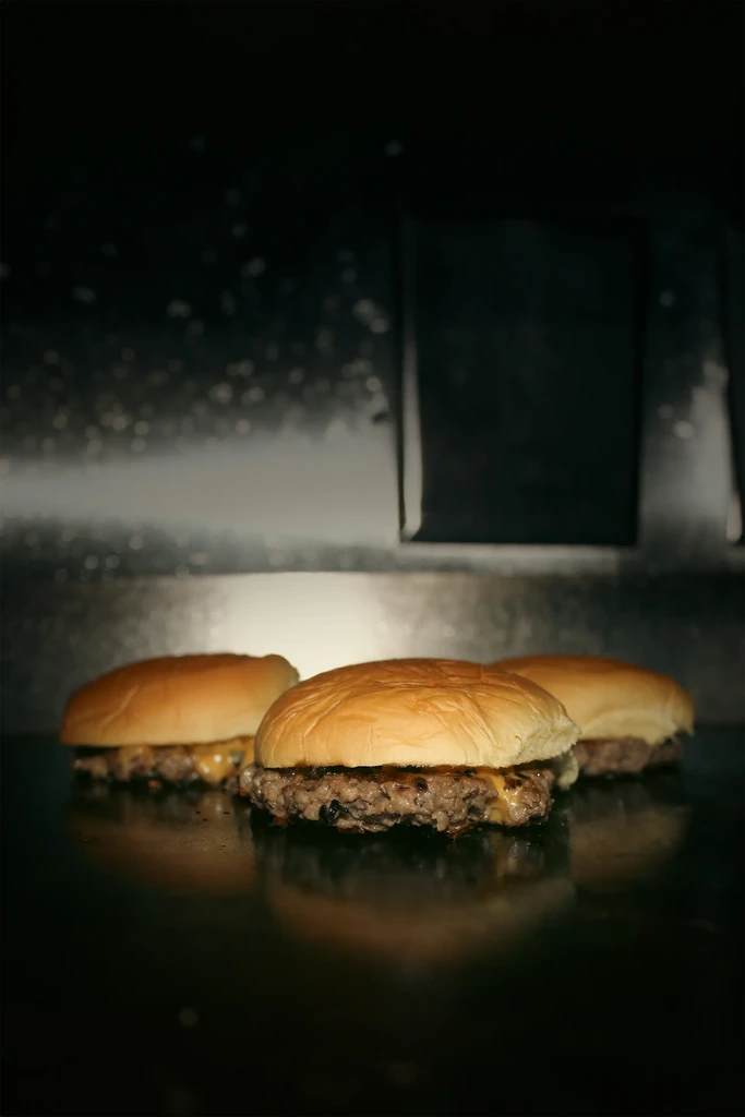 Three grilled cheeseburgers with melted cheese on a dark, reflective surface.