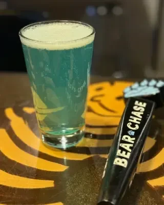 Two-toned teal and yellow drink with foam, next to 'Bear & Chase' tap.