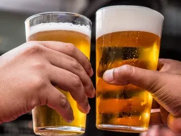 Hands clinking clear glasses of golden beer with frothy heads.