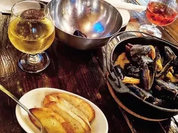 Mussels, bread, and drinks on a rustic dark wooden tabletop.