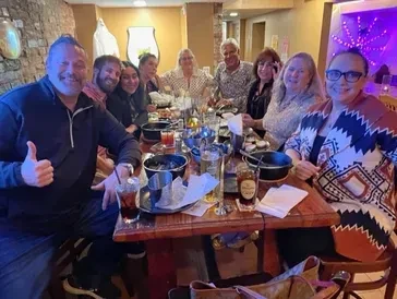 Ten smiling adults enjoying a meal at a cozy, rustic restaurant.