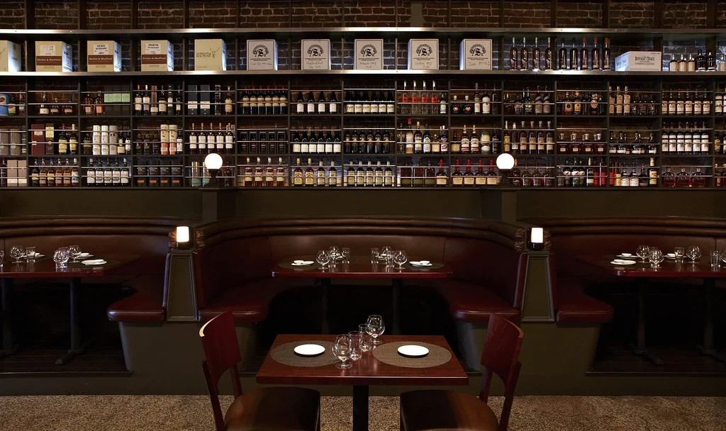 Restaurant bar interior: brick wall, liquor display, red booths, set tables.