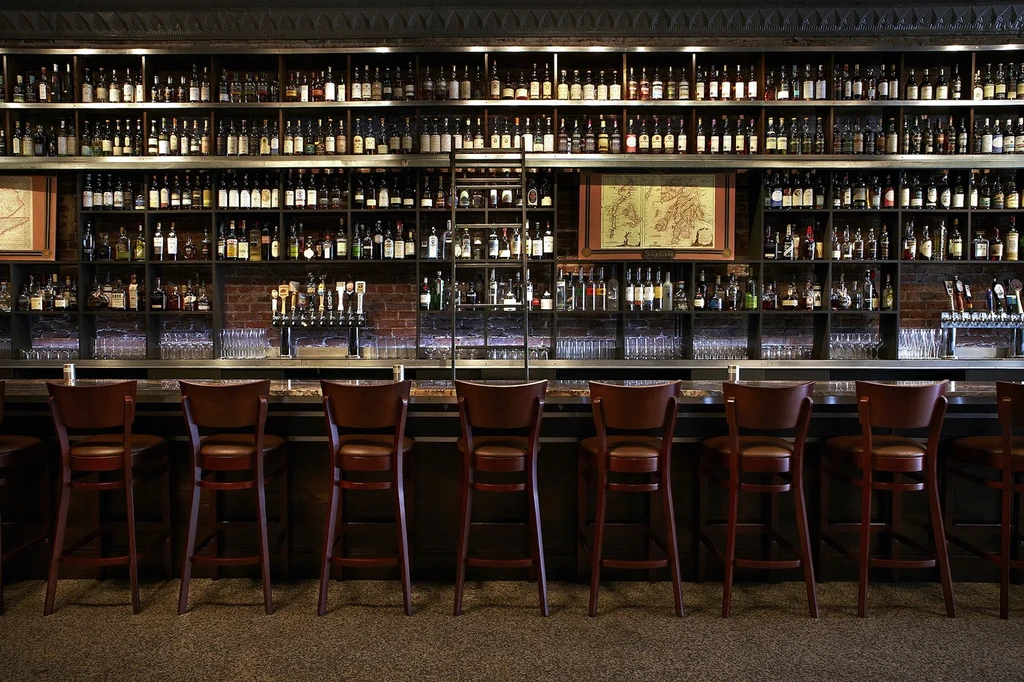 Restaurant bar with extensive bottle shelves, beer taps, and unoccupied stools.