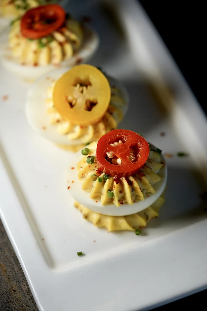 Three deviled eggs with red and yellow tomatoes, chives, and paprika.