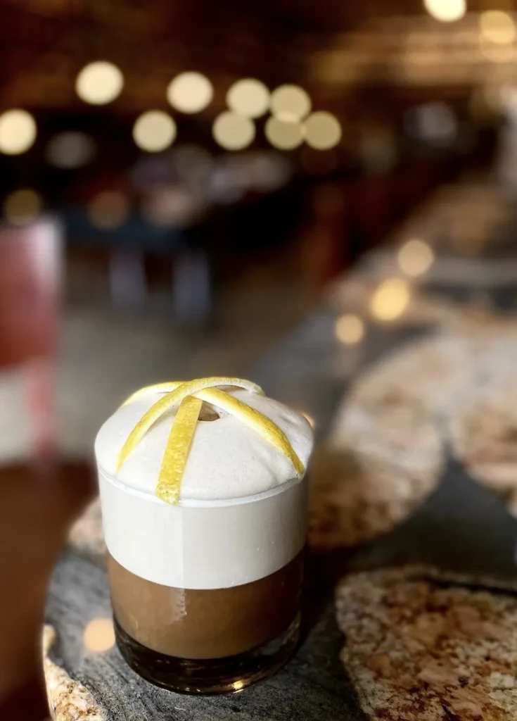 Dark drink with white foam and lemon peel lattice.