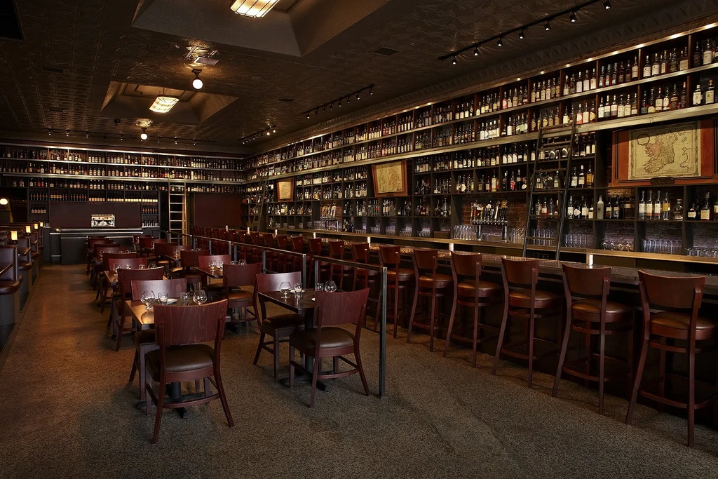 Spacious restaurant interior featuring a tall, bottle-lined bar and seating.