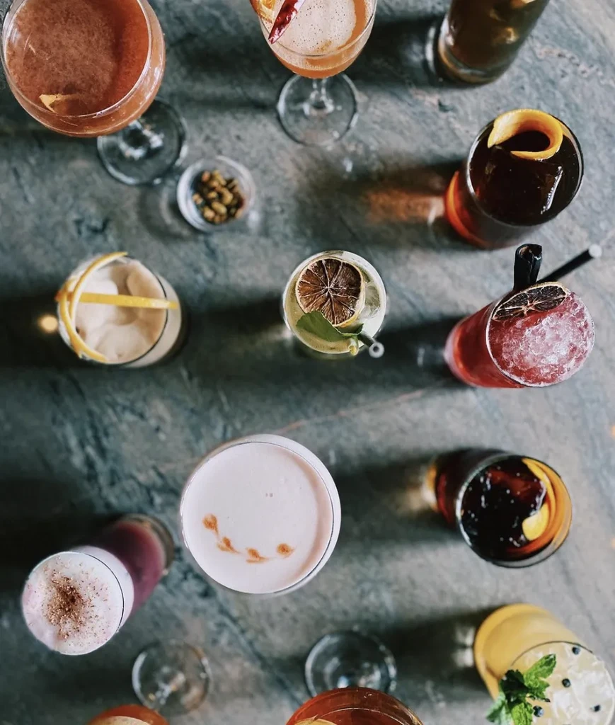 Variety of garnished cocktails, overhead on a dark mottled stone.