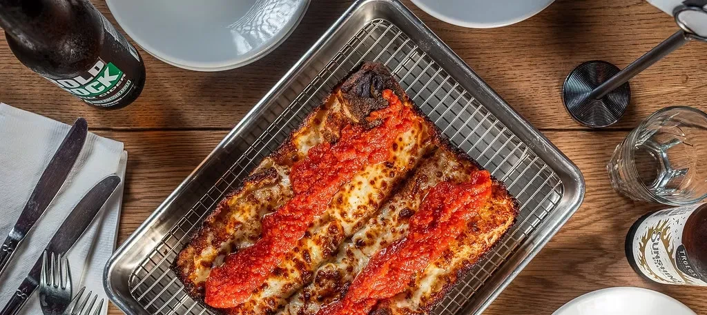 Rectangular pizza in a metal tray with melted cheese and sauce stripes.
