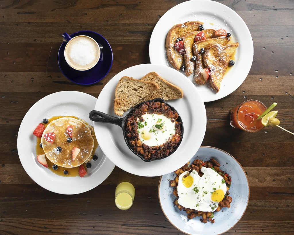 Overhead: Wooden table laden with diverse breakfast and brunch dishes.