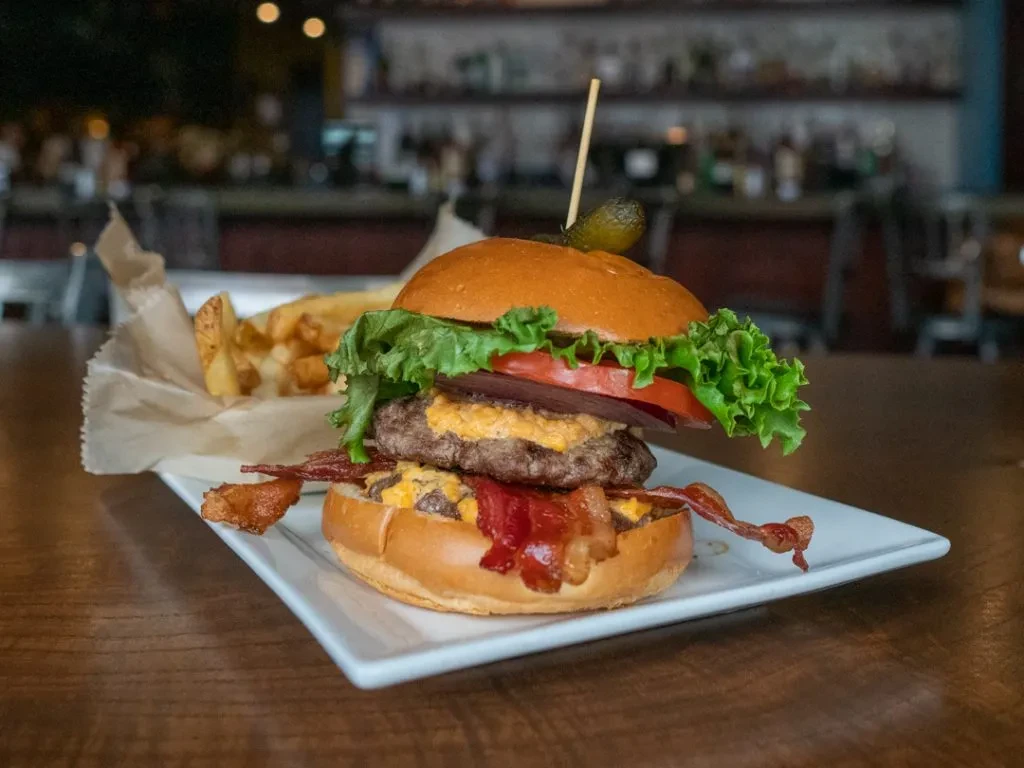 Double bacon cheeseburger with pickle, fries on a wooden table.