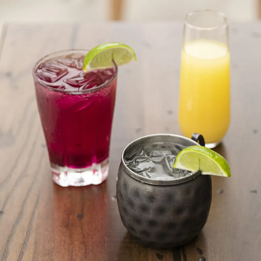 Purple, clear, and yellow cold drinks on a rustic wooden table.