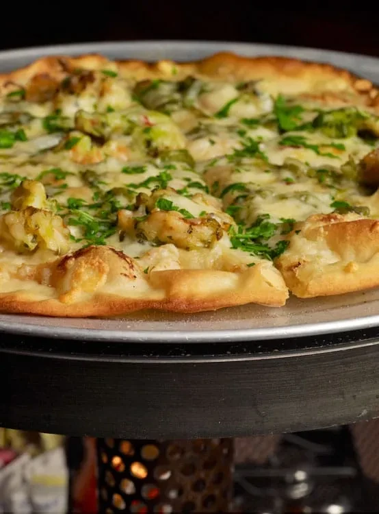 Close-up of baked pizza with melted cheese, vegetables, herbs, and pulled slice.