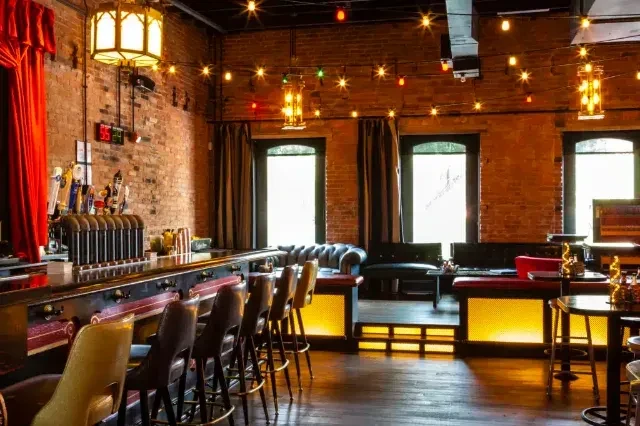 Restaurant bar interior with a wooden counter, brick walls, and string lights.