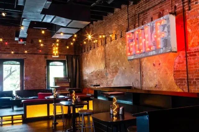 Rustic bar interior with brick walls, string lights, and illuminated 'BAR' sign.