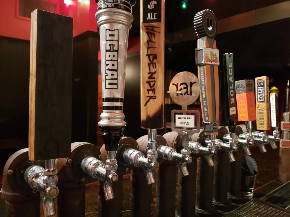 Multiple beer taps with various craft brewery handles in a dim bar.