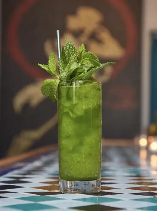 Vibrant green muddled drink with mint, straw, on tiled surface.