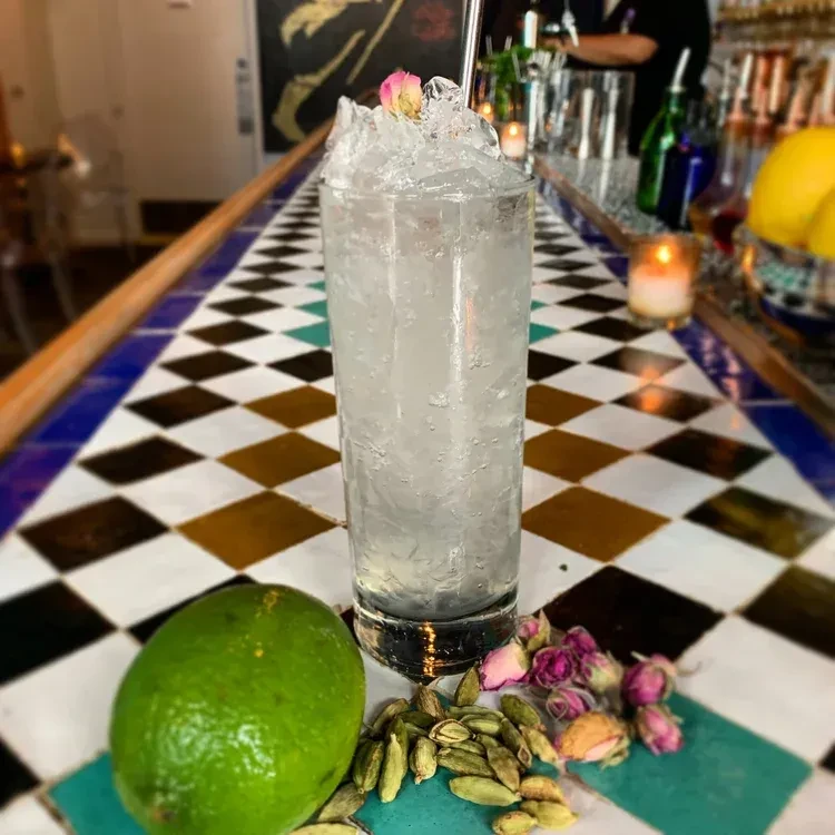 Rosebud-garnished cocktail with lime and cardamom on a checkered bar.