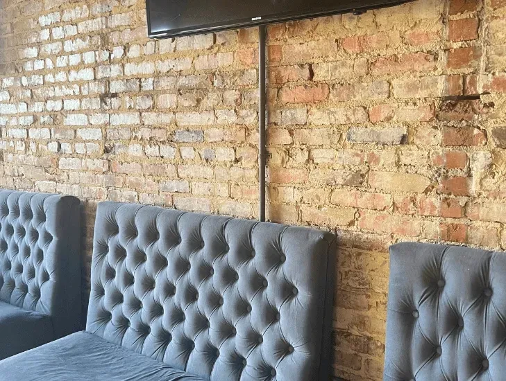 Interior with dark tufted booths, exposed brick wall, and TV.