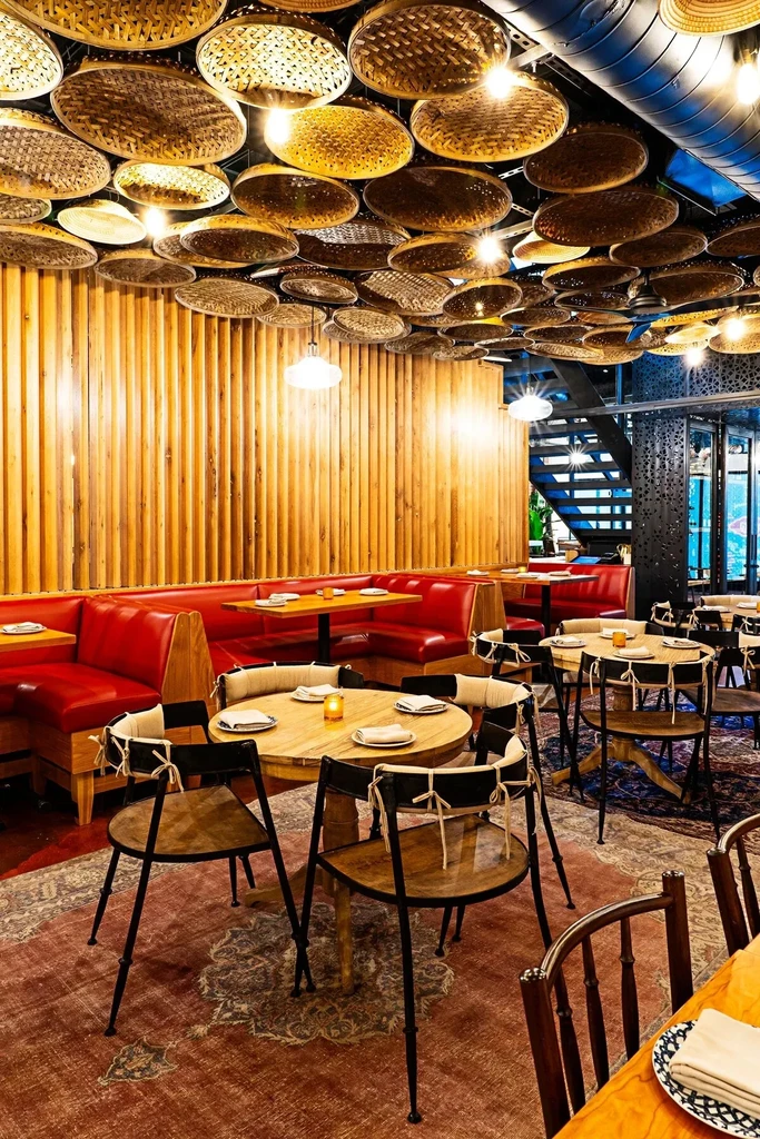 Restaurant interior with wooden tables, red banquettes, and glowing rattan ceiling.