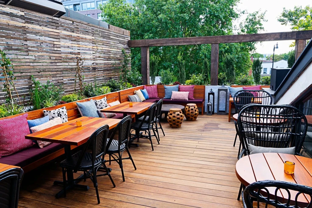 Outdoor wooden patio dining with colorful cushions and green foliage.