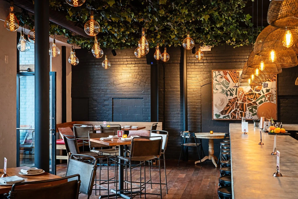 Modern restaurant with lush foliage, Edison bulbs, and dark brick walls.