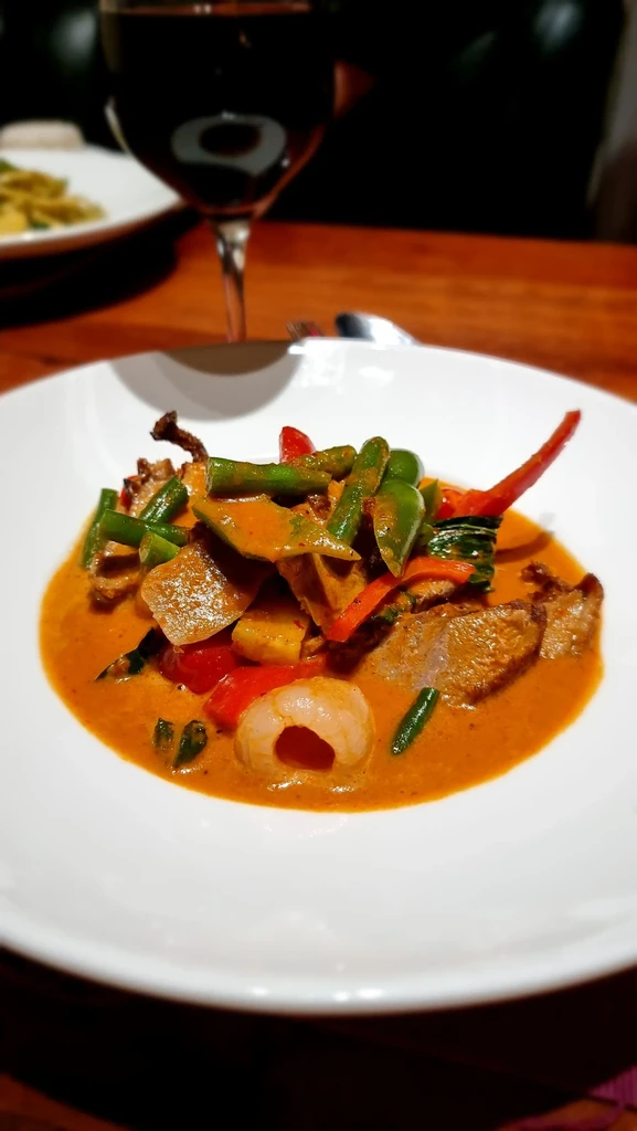 Close-up of reddish-orange curry with meat, vegetables, pineapple, and lychee.