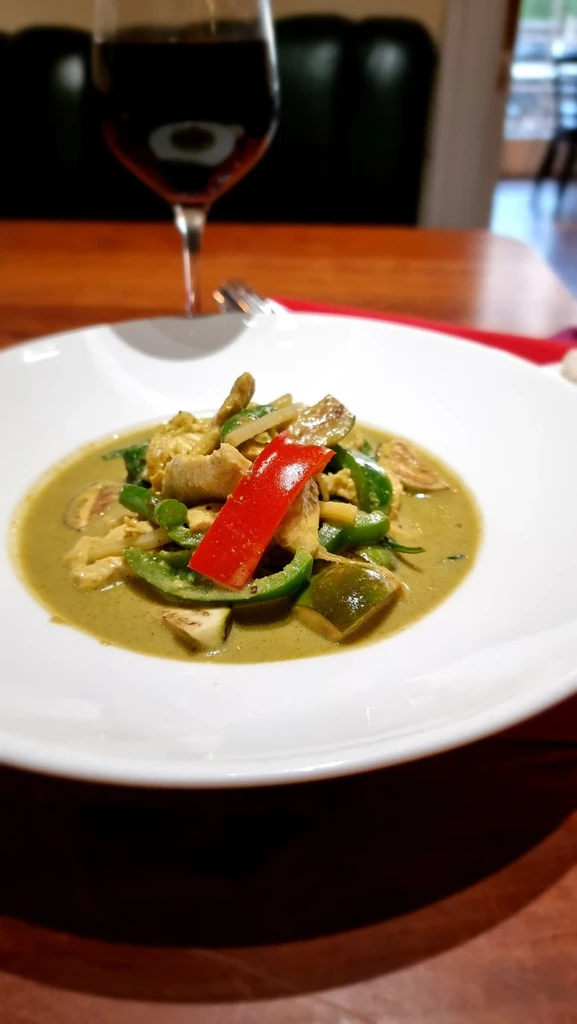 Green curry with chicken, vegetables, red pepper, in a white bowl.