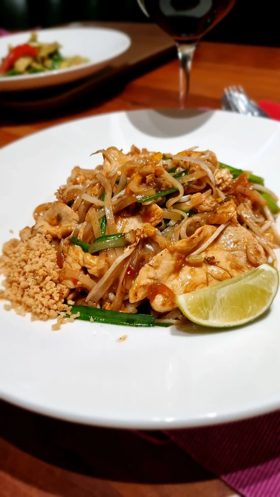 Chicken Pad Thai with noodles, peanuts, and lime on a white plate.