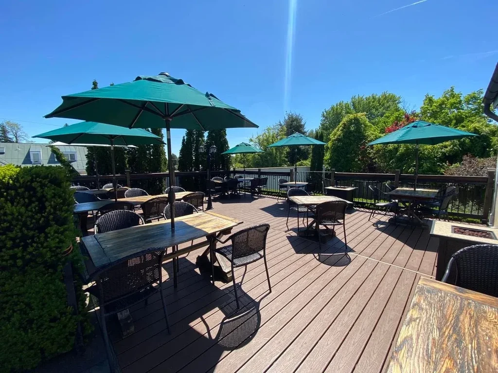 Empty sunny restaurant patio with tables, wicker chairs, and umbrellas.