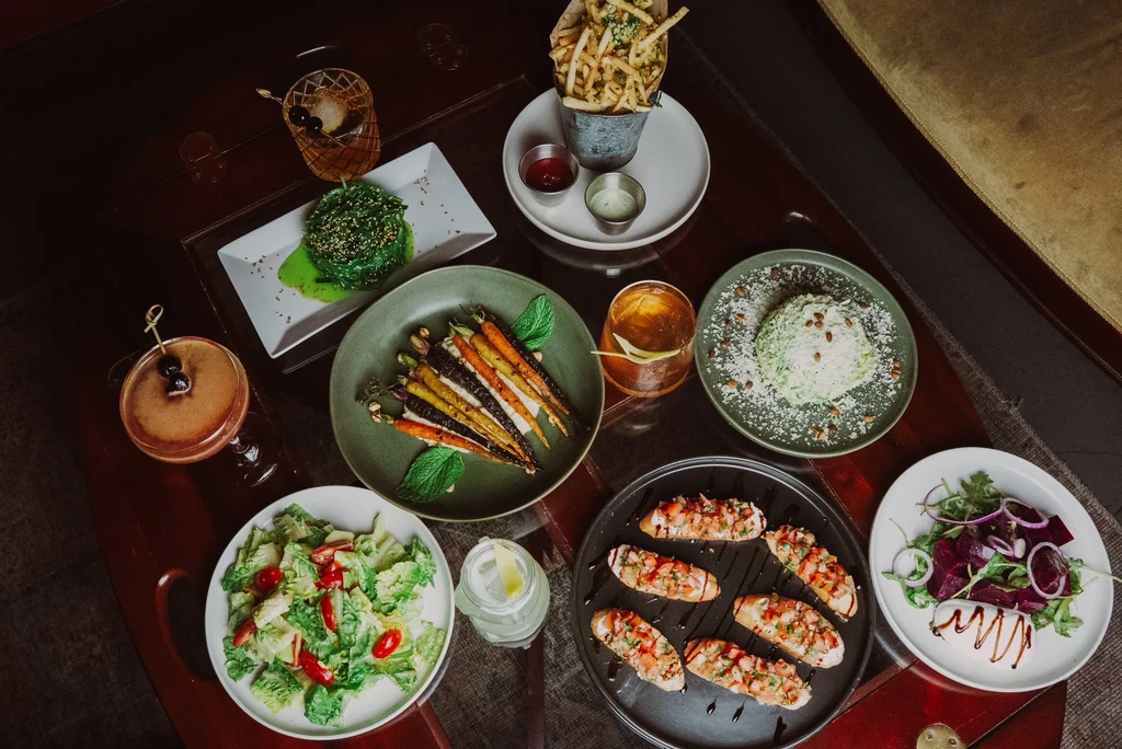 Overhead view of a dark wooden table laden with food and cocktails.