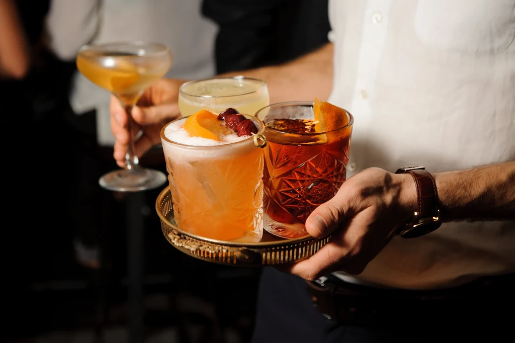 Three distinct cocktails on a golden tray, held by a server.