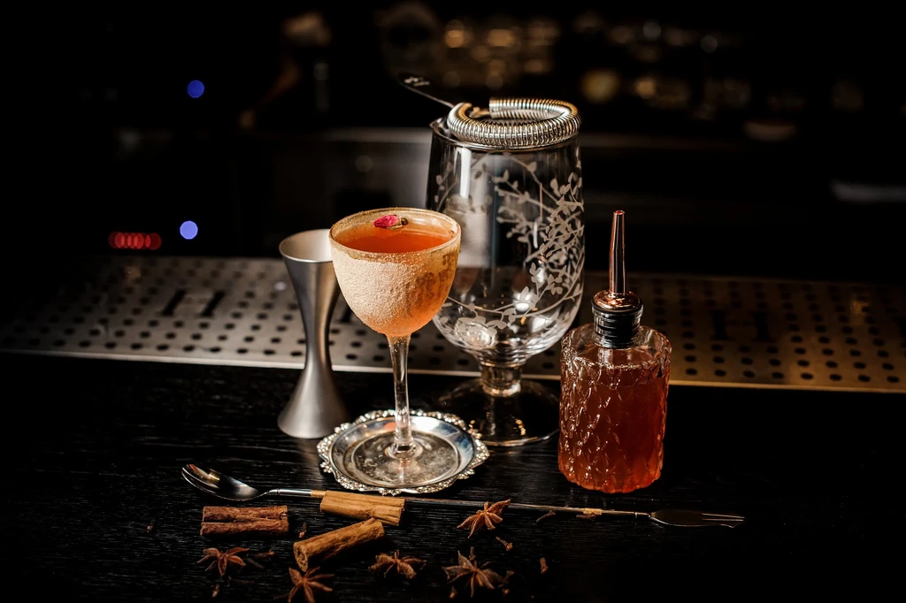 Elegant amber cocktail with rosebud, bar tools, and spices.