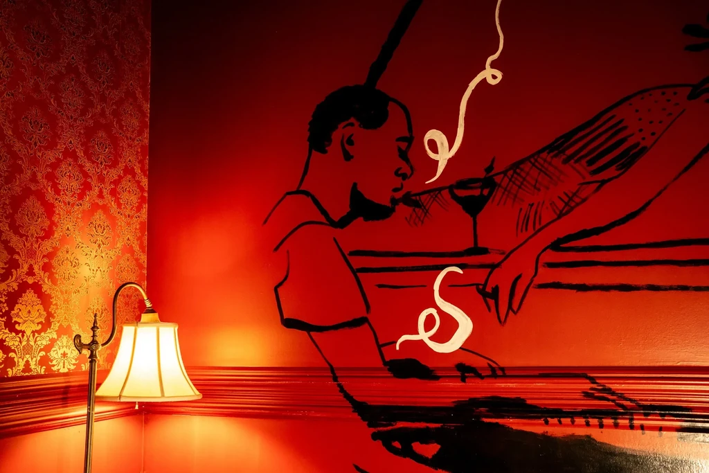 Red damask wallpaper, floor lamp, and stylized man mural with drink.