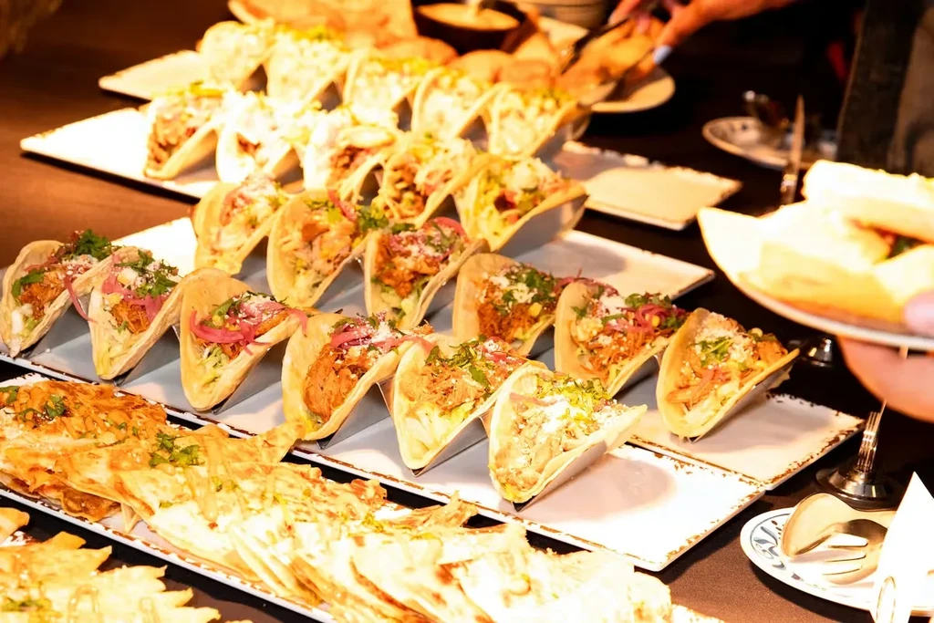Buffet with rows of various tacos, quesadillas, and serving hands.