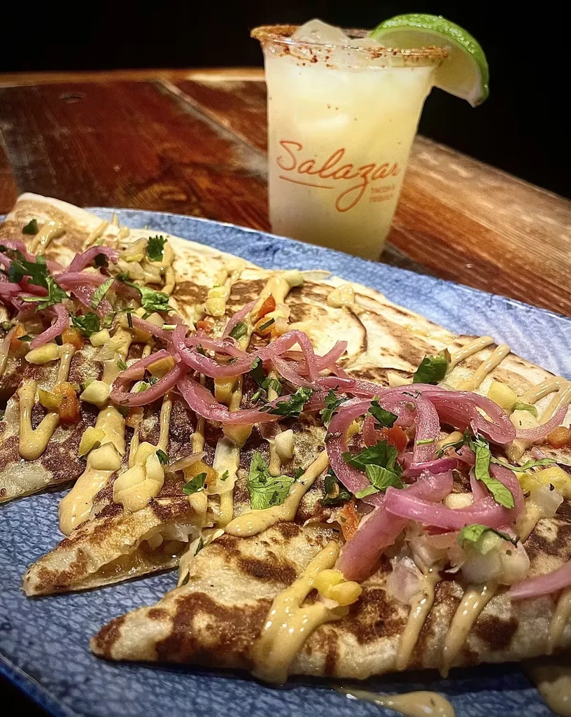 Topped quesadilla slices and a spice-rimmed drink with a lime.