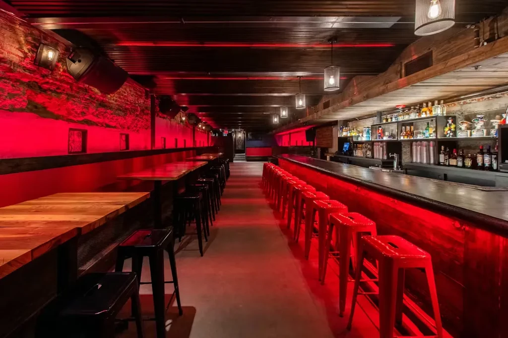 Modern bar interior with red ambient lighting, long bar counter, and stools.
