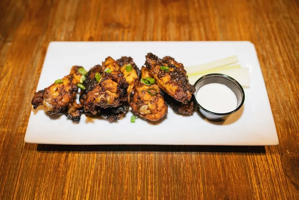 Plate of crispy chicken wings with green onions, dipping sauce, and celery.