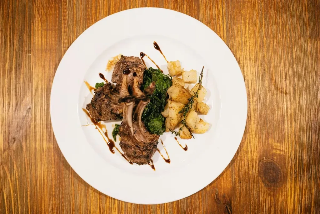 Roasted lamb chops with bones, green vegetables, potatoes, sauce on a plate.