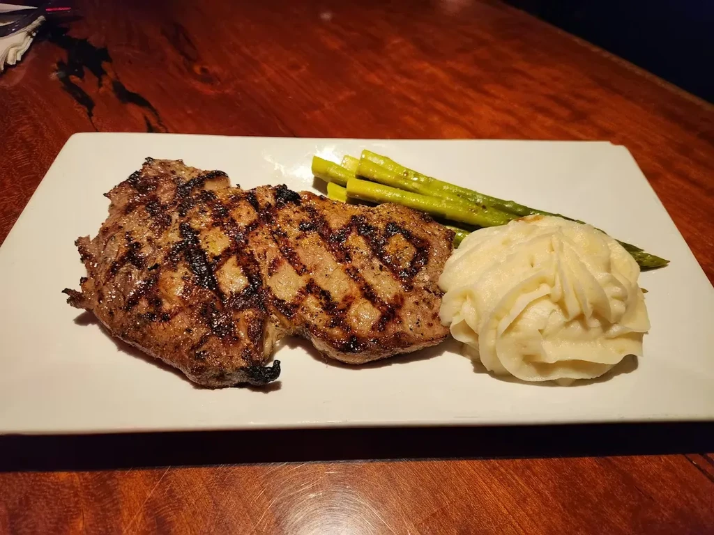 Charred grilled steak, green asparagus, and mashed potatoes on a white plate.