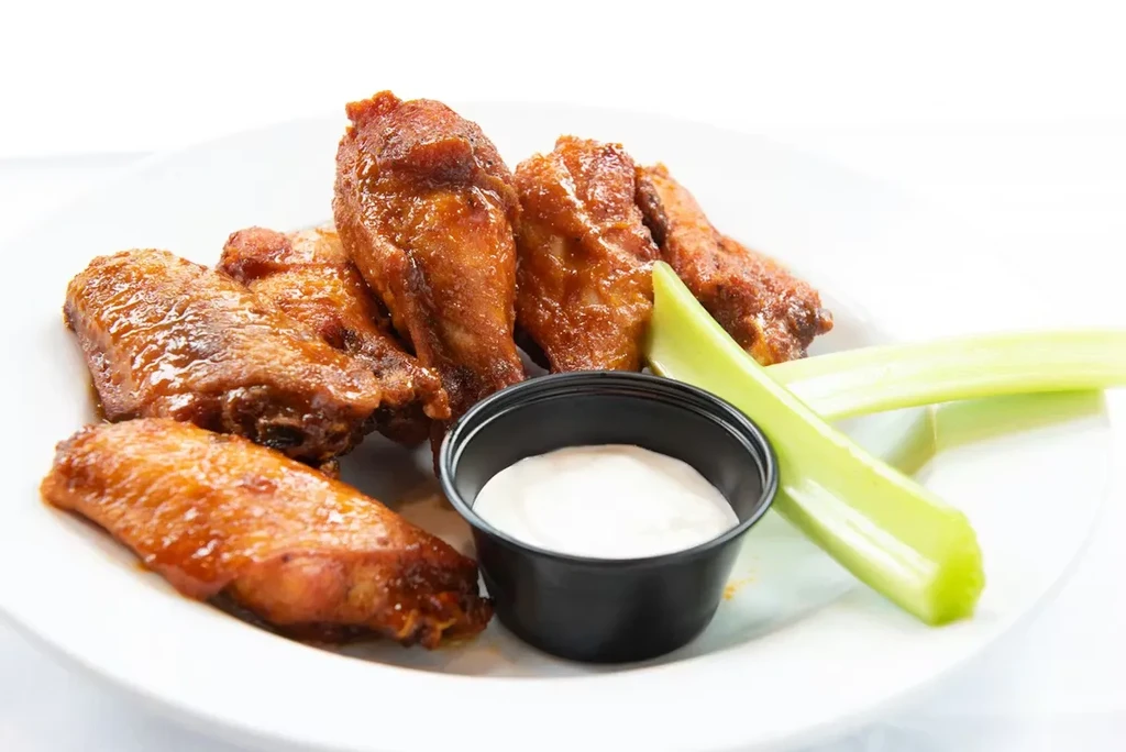 Plate of Buffalo chicken wings with dipping sauce and celery.