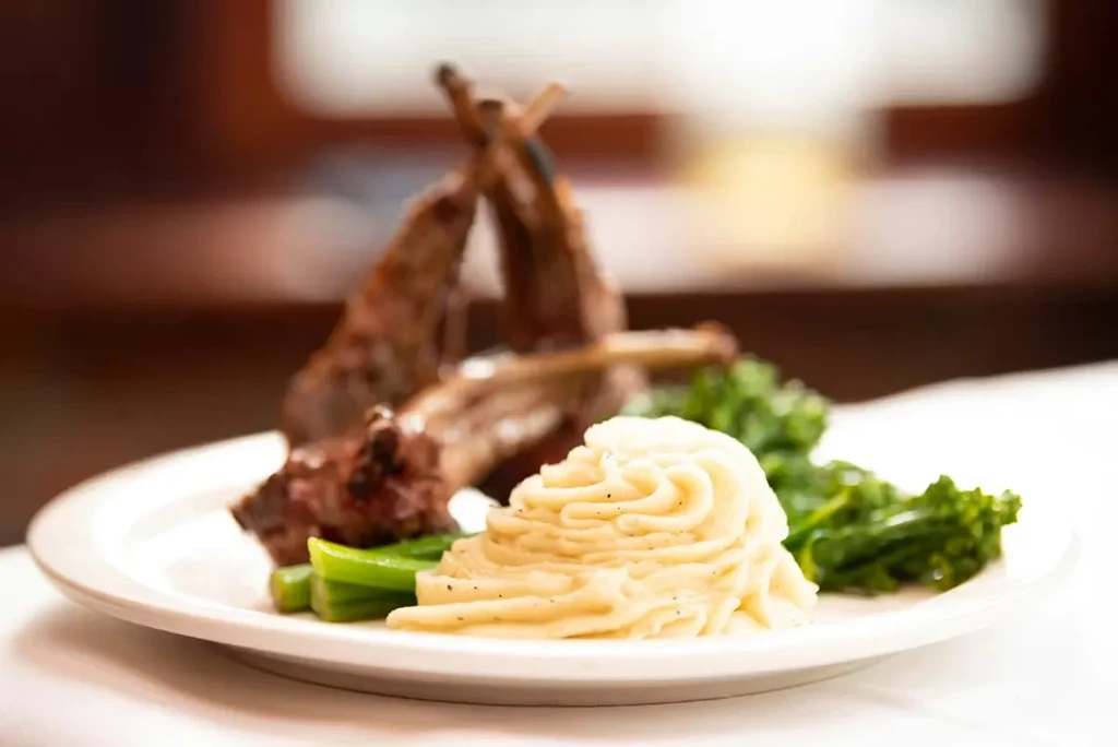 Beautifully plated lamb chops, mashed potatoes, and green vegetables.