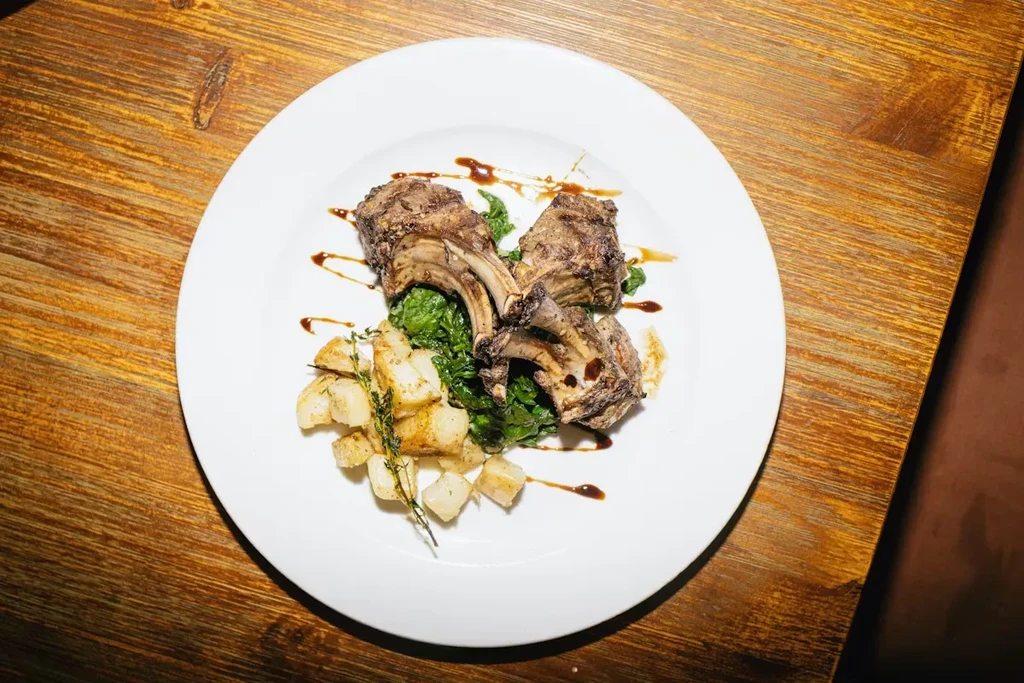 Artfully plated lamb chops, greens, potatoes, and sauce on wood.