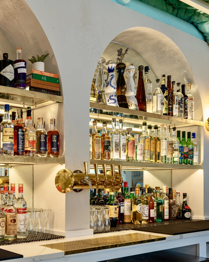 Elegant bar interior showcasing numerous bottles, brass taps, and a marble counter.