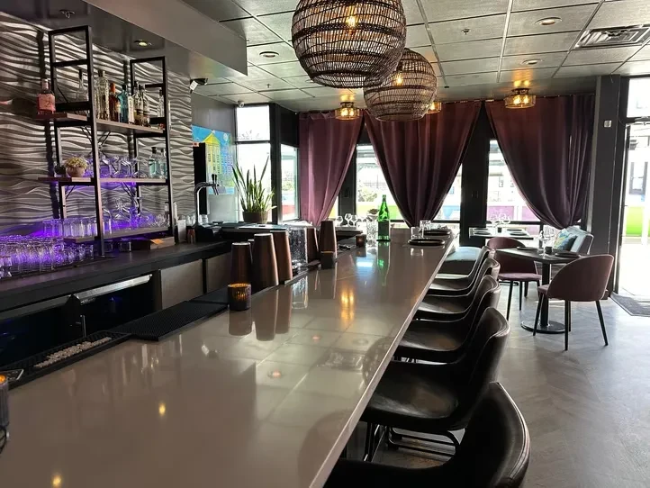 Modern bar counter, stools, purple-lit liquor shelves, and dining tables.